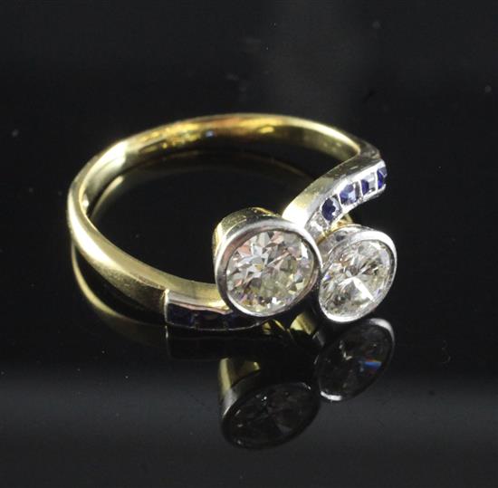 An 18ct gold and two stone diamond cross-over ring with square cut sapphire set shoulders, size U.